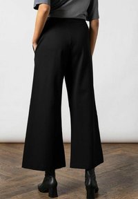 Zwarte wijde broek gemaakt van soepele stof, met een hoge taille en zijzakken, gecombineerd met zwarte enkellaarsjes.
