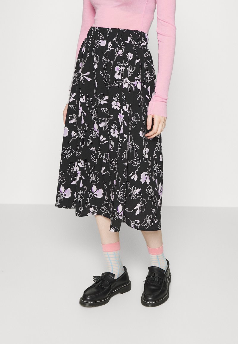 Saia preta com padrões florais em roxo, com cintura elástica, design até aos joelhos. Combinada com uma blusa rosa e meias estampadas. Sapatos pretos.