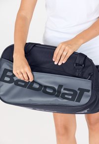 Bolsa deportiva negra y gris con un gran logo negro, que cuenta con un bolsillo con cremallera y material texturizado. Las asas son resistentes para un transporte fácil.
