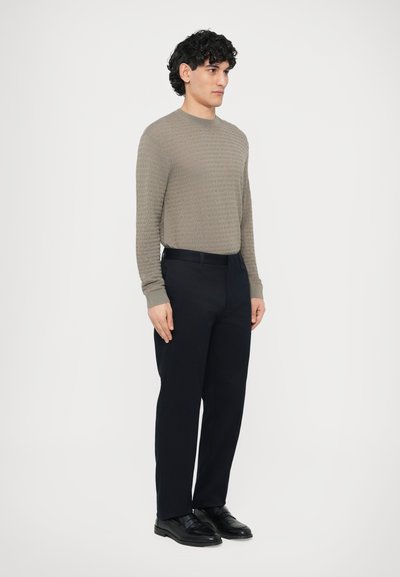 Jasnoszary sweter o fakturowanej strukturze z długimi rękawami, zestawiony z granatowymi spodniami i czarnymi eleganckimi butami. Prosty i uporządkowany design.