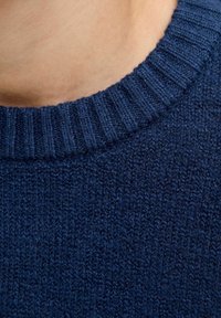 Jūras spēku zila adīta džemperis ar ribotu apkakli. Auduma struktūra ir maiga, ar blīvu un vienmērīgu pinumu, kas rāda vienmērīgu krāsu visā džemperī.