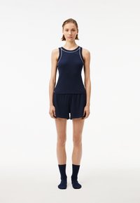 Tricou sportiv de culoare bleumarin, cu cusături albe de accent, asortat cu pantaloni scurți și șosete bleumarin. Textură netedă, design ajustat, stil minimalist.