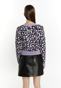 Maglione lavorato a maglia con sfondo nero e motivo floreale viola, colletto e orlo a coste color lilla, abbinato a una gonna in pelle nera.