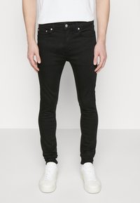 Jean skinny noir avec design à cinq poches, confectionné en denim. Dispose d'un bouton argenté et de coutures contrastées. Associé à des baskets blanches.