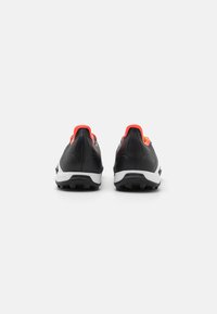 Zwarte sportieve schoenen met rode accenten, gestructureerde bovenkant en witte zool. Voorzien van een gepolsterde hiel en multidirectionele grip-noppen.