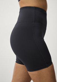 Højtaljede sorte shorts lavet af glat, strækbart stof med flade sømme, der omfavner lårene og giver en tætsiddende silhuet.