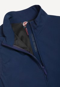 Μπλε σκούρο μπουφάν Colmar Originals με μερικώς ξεκλειδωμένο μπροστινό μέρος που δείχνει μαύρη εσωτερική επένδυση και επωνυμικό ετικέτα στο εσωτερικό γιακά.