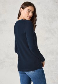 Maglione navy a maniche lunghe con lavorazione a maglia testurizzata, scollatura rotonda e vestibilità slim, abbinato a jeans blu, visto da dietro.