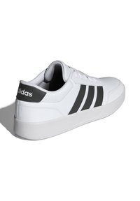 Bijele tenisice s crnim Adidas logotipom i tri crne pruge. Gornjište od glatke kože, gumeni potplat, dizajn na vezivanje, podstavljena ovratnik.