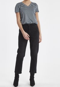 Camiseta de cuello en V de manga corta a rayas en gris y negro, combinada con unos jeans de cintura alta negros y botas negras hasta el tobillo.