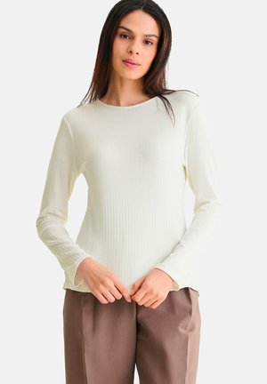 Licht crèmekleurig geribbeld shirt met lange mouwen en een ronde halslijn, zachte textuur en een relaxed fit, gecombineerd met bruine broeken.