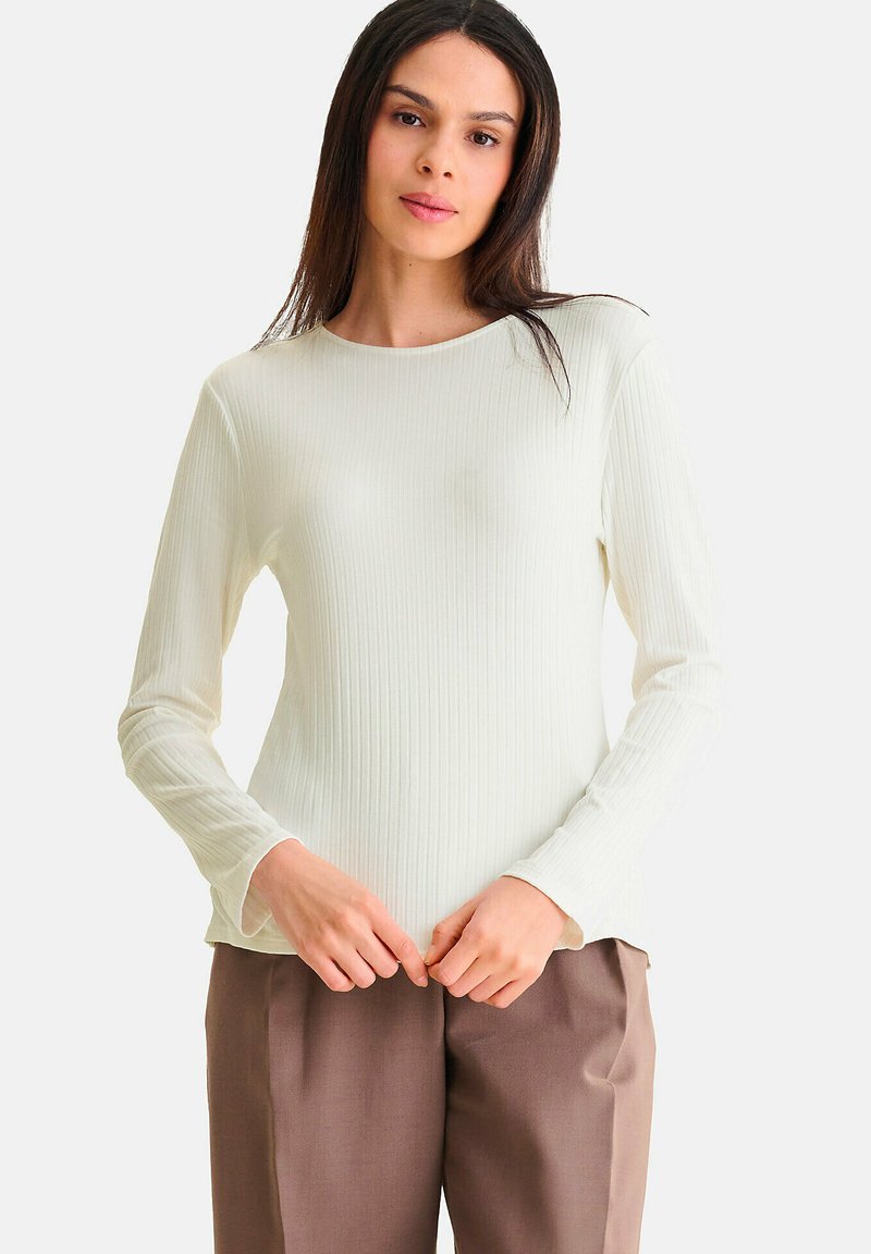 Licht crèmekleurig geribbeld shirt met lange mouwen en een ronde halslijn, zachte textuur en een relaxed fit, gecombineerd met bruine broeken.