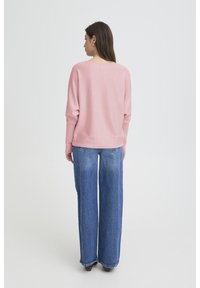 Pull rose clair à manches longues et coupe ample, associé à un jean bleu taille haute à jambes larges. Texture douce et design décontracté.