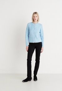 Ljusblå texturerad cardigan med ett diamantt mönster och runda knappar, bärs över svarta skräddarsydda byxor och ankle boots.