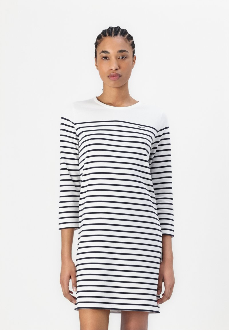 Rochie stripedă în alb și navy, cu un decolteu rotund și mâneci trei sferturi. Include un mic logo al mărcii pe piept.