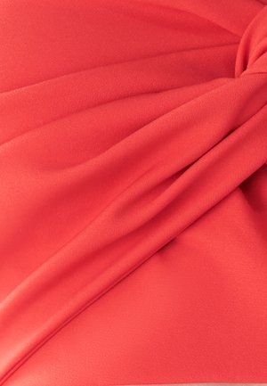 Roter Stoff mit weicher Textur, der gefaltete Drapierungen und eine geknotete Akzentuierung aufweist. Das Material wirkt leicht und glatt.