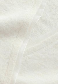 Soft, white textured knit fabric with a semi-transparent, shiny edging detail, showing close-up of overlapping layers.