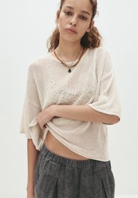 Hellbeige Strickoberteil mit weiten, kurzen Ärmeln und lockerem Schnitt, kombiniert mit dunkelgrauen Jogginghosen mit Kordelzug und weichem Material.