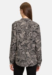 Lange mouwen shirt van zwarte stof met een beige paisley- en bladenpatroon. Klassieke kraag en knoopmanchetten, gebogen zoom aan de achterkant.