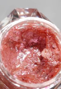 En klar glasskrukke som inneholder en tykk, glitrende, rødlig-pink skrubb med en grov tekstur, som avdekker biter av skimmer gjennom hele.