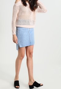 Jasnoróżowy, sweter o otwartym splocie z fasonem odkrytych ramion, zestawiony z jasnoniebieską spódnicą dżinsową z surowym wykończeniem i bocznym rozcięciem, noszony z czarnymi klapkami.