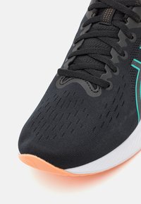 Chaussure de sport noire avec un dessus en mesh respirant, des accents turquoise et une semelle en caoutchouc avec un talon de couleur pêche.