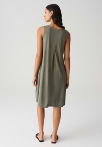 Sleeveless olive green dress with a straight cut, featuring a back pleat. Soft, smooth fabric and mid-thigh length. Slip-on style.