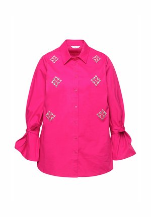 Světlé růžové tričko s designem na knoflíky, které má dekorativní vzory z rhinestones na přední straně a objemové, zavázané rukávy.