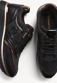 Black sneakers with a smooth leather finish, mesh accents, and metallic bronze details. Features laces and a side zipper for easy wear.