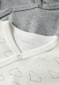 Kaksikud imikute bodysuiti: üks halla ribidega kraega, teine valge pilvemustriga. Mõlemal on kaela juures surveklapid.