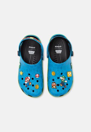 Niebieskie buty Crocs z nadrukowanymi postaciami i ikonami z Super Mario, w tym Mario, Luigi, monetami, grzybami i gwiazdkami na cholewce.
