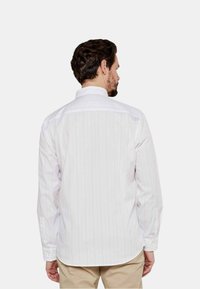 Camicia bianca a maniche lunghe con strisce verticali rosa chiaro, colletto classico e orlo curvo, realizzata in un morbido tessuto misto cotone.