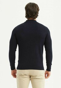 Pull en tricot bleu marine à manches longues et col rond. Présente une texture lisse, des poignets et un ourlet côtelés.