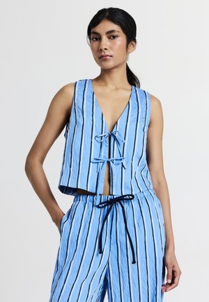 Donna che indossa un top senza maniche a righe verticali blu e bianche con lacci davanti e pantaloni coordinati con coulisse, su sfondo bianco.