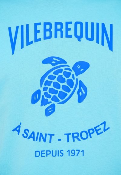 Turkizna majica s plavim grafičkim uzorkom kornjače. Sadrži natpis "VILEBREQUIN" i "À SAINT-TROPEZ" u podebljanom plavom slovu. Glatka tekstura.