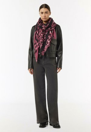 Ein pink- und schwarz gemusterter Schal, der über einer schwarzen Lederjacke drapiert ist, kombiniert mit hochgeschnittenen dunklen Jeans und schwarzen Stiefeln.