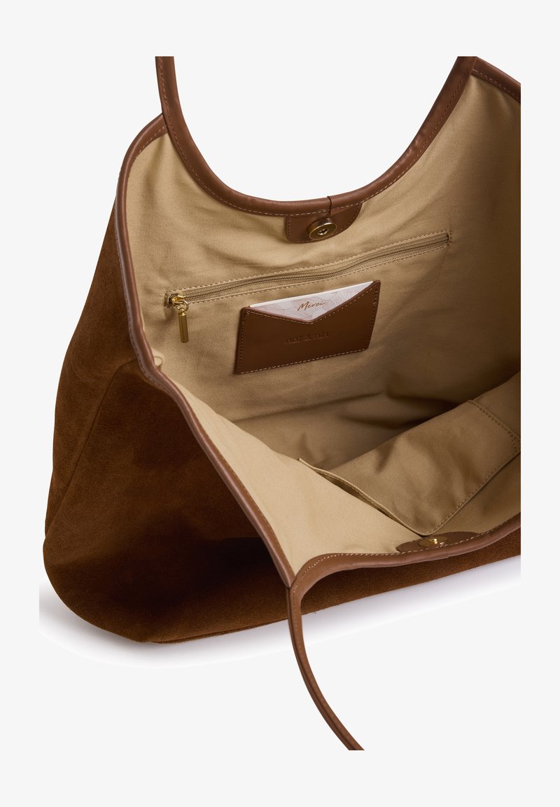 Sac cabas en suède marron avec détails en cuir. L'intérieur est doté d'une doublure beige, d'une poche zippée et d'un emplacement pour carte. Spacieux avec des bords arrondis.