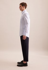 Camicia a righe blu chiaro a maniche lunghe con taschino, abbinata a pantaloni scuri e scarpe eleganti nere, vista di lato.