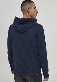 Dunkelblauer Hoodie mit einer Kapuze mit Kordelzug, gerippten Bündchen und einem gerippten Saum. Hergestellt aus weichem Stoff und mit einer dezenten Textur.