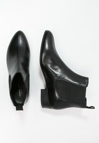 Botas de cuero negras hasta el tobillo con puntera puntiaguda, paneles laterales elásticos y un tacón bajo apilado. Textura suave y diseño minimalista.