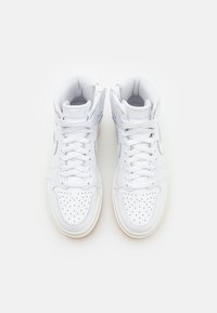 Paire de baskets montantes blanches avec embout perforé et lacets blancs, vue de dessus sur un fond uni.