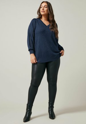 Suéter azul marino con cuello en V, patrón de chevron texturizado, mangas ajustadas, combinado con pantalones negros ajustados y botines.