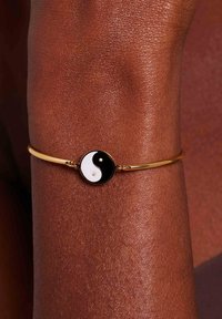 Bracelet en or avec un symbole yin-yang noir et blanc circulaire, agrémenté de deux petites pierres qui soulignent le design.