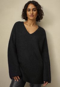 Sort oversized sweater lavet af blødt, fluffy materiale med dyb V-hals og lange ærmer, med en afslappet pasform og sideslidser.