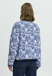 Quiltad jacka med ett blått och vitt paisleymönster, långa ärmar, rund hals och en cropped design. Tillverkad av strukturerad tyg.