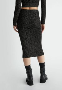 Gonna nera in maglia con un motivo geometrico ripetuto, lunghezza fino al polpaccio, caratterizzata da una texture a coste e una silhouette aderente.