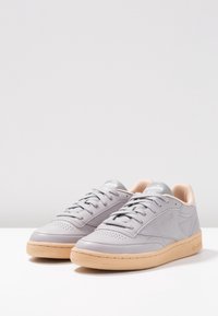 Hellgraue Ledersneaker mit glatter Oberfläche, runder Zehe und beiger Gummisohle. Mit Schnürung und einem silbernen Logo auf der Zunge.