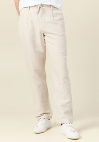 Ljusbeige linnebyxor med en avslappnad passform, med dragsko i midjan, sidelommor och en mjuk textur. Matchas med vita sneakers.