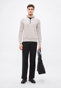 Helehall zip-kaelusega kampsun soonikkoes varrukate ja äärega, kombineeritud mustade pükste ja musta kandekotiga. Sile tekstuur, minimalistlik disain.