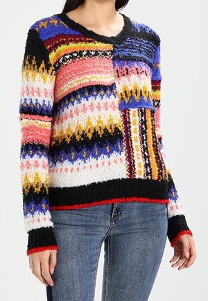 Colorful knit sweater with mixed geometric patterns in blue, pink, yellow, black, and red paired with blue jeans on a person.